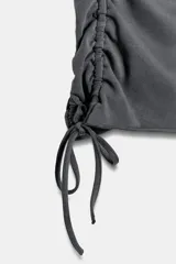 Camiseta corta de cuello redondo y manga corta, color gris oscuro, con frunces laterales ajustables mediante cordones.