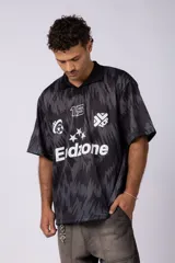 Camiseta de estilo futbolero con cuello polo, manga corta y corte relajado. Presenta un estampado abstracto en tonos grises y negros, con el número 15, el logo de la marca y la palabra Endzone en el frente.