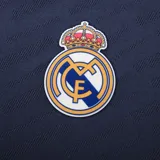 Camiseta de fútbol azul marino con cuello redondo y mangas cortas. Presenta un patrón de líneas diagonales en relieve y el escudo del Real Madrid bordado en el pecho.