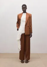 Pantalón de vestir estilo sastre color marrón, de corte recto, tiro bajo, con bolsillos laterales y cierre frontal de botón, gancho y cremallera.