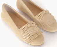 Mocasín de cuero gamuzado color avena, con detalle de flecos en la capellada y un lazo frontal con herrajes metálicos dorados. Cuenta con interior forrado en cuero y suela de goma flexible.