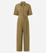 Mono enterito de color verde militar, confeccionado en viscosa y poliamida, con cuello alto decorado con un lazo, mangas cortas, bolsillos aplicados en el pecho y cintura con presillas y cinturón integrado con botones. Las piernas son amplias y de corte recto.