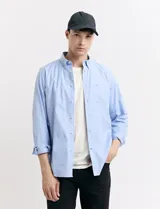 Camisa de corte clásico confeccionada en tejido oxford, con diseño de rayas verticales en tonos azul y blanco. Presenta cuello abotonado, cierre frontal con botones y bolsillo en el pecho con detalle de etiqueta bordada.