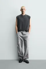 Pantalón de jean estilo carpintero con corte relaxed fit, tiro medio y pierna recta. Presenta un lavado azul medio con efecto desgastado y roturas en las rodillas. Incluye bolsillos laterales tipo plastrón, tira multifunción en la pierna, cierre frontal con cremallera y botón.