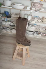 Bota alta de gamuza marrón, con diseño de doble caña, punta cuadrada y taco bajo. Cuenta con cierre lateral.