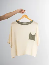 Remera tejida color crema con cuello redondo y bolsillo frontal verde.
