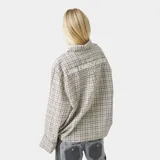 Camisa de manga larga con corte boxy fit, confeccionada en tela a cuadros en tonos beige y marrón. Presenta cuello clásico, cierre frontal con botones y un bolsillo en el pecho con el logo de la marca bordado.