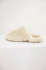Pantufla tipo slip-on confeccionada en piel de cordero (babylamb) color beige, con diseño bordado del logo en la capellada y suela plana.