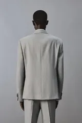 Blazer slim fit de color gris, con cuello de solapas de muesca, cierre frontal de dos botones, bolsillos laterales con solapa y bolsillo de vivo en el pecho. Presenta mangas largas con botones en los puños y aberturas en la espalda.