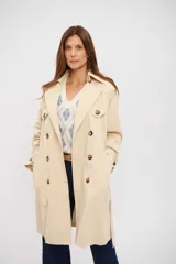 Trench coat color beige de corte clásico, con doble botonadura frontal, solapas anchas, cinturón ajustable con hebilla y trabillas en los puños.
