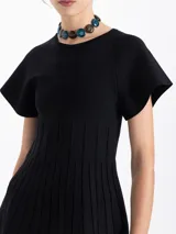 Top de tejido de punto color negro, con cuello redondo, mangas cortas acampanadas y cuerpo con diseño de tablas verticales que aportan estructura.