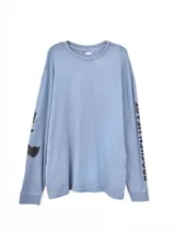 Remera de manga larga en color azul grisáceo con efecto lavado. Presenta un diseño holgado y estampado gráfico en color negro en ambas mangas, incluyendo texto en una de ellas.