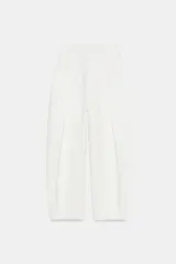 Pantalón balloon de tiro alto color blanco con pliegues en la parte delantera, bolsillos laterales ocultos y cierre frontal con cremallera, botón interior y ganchos metálicos.