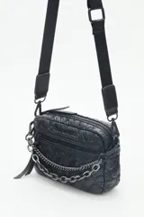 Bandolera pequeña de nylon acolchado con patrón de corazones, color rojo brillante. Posee correa regulable, cierre principal y bolsillo frontal con cierre. Incluye un llavero colgante con dije de corazón.