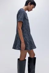 Vestido corto de tejido bouclé en tonos azul marino y blanco, con cuello redondo, manga corta y cierre frontal con botones metálicos decorativos. La falda tiene un corte acampanado con vuelo.