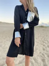 Camisola negra larga de lino con cuello camisero, cierre frontal con botones dorados, bolsillo de cuero dorado en el pecho y puños con detalle de cuero dorado.