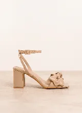 Sandalia de taco alto cuadrado, color beige con acabado acharolado, puntera cuadrada y un llamativo detalle de nudo en la tira delantera. Cuenta con tira ajustable al tobillo con hebilla.