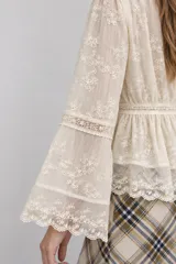 Blusa marfil con detalles de encaje y bordados florales transparentes, con escote en V, cierre frontal abotonado y mangas largas acampanadas.