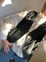 Chaleco de cuero negro sin mangas, con escote en V, cierre frontal de botones y detalles de flecos colgantes en el frente.