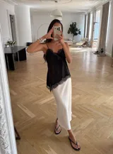 Blusa de satén negro con delicados breteles finos y terminaciones de encaje en el escote y el ruedo, de silueta fluida y calce relajado.