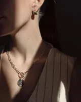 Collar de cadena de eslabones alargados con cierre frontal tipo T y dije circular de textura rústica e irregular.