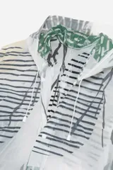 Piloto impermeable de corte recto y largo midi, con capucha ajustable mediante cordones. Presenta un diseño estampado con motivos botánicos en tonos verdes y amarillos sobre una base translúcida. Cuenta con cierre frontal mediante botones a presión y mangas largas.