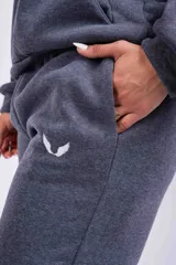 Pantalón de jogging gris oscuro, de corte holgado con cintura elástica y puños ajustados en los tobillos. Presenta bolsillos laterales y un pequeño logo bordado en la pierna izquierda.