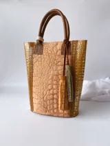 Bolso matero de cuero color beige con textura tipo piel de cocodrilo, detalles en cuero color marrón y borlas decorativas.
