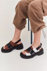 Sandalias de plataforma con suela track negra. Presentan un diseño de tiras anchas combinadas en cuero con textura de reptil color marrón y una franja central de charol negro. Incluyen una tira trasera elástica para mayor sujeción.