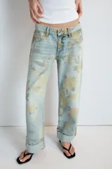 Jeans de tiro bajo confeccionados en denim, con diseño holgado y estampado integral de rosas en tonos amarillos y verdes sobre fondo celeste claro. Cuenta con cinco bolsillos, trabillas para cinto y botamangas con vuelta.