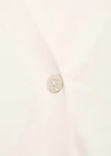 Cardigan de punto fino color crema, con cuello en V, cierre frontal con botones y mangas largas con puños acanalados.