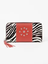 Billetera rectangular de cuero con cierre perimetral, diseño combinando laterales de pelo con estampado animal print tipo cebra y franja central roja con tachas metálicas dispuestas en forma circular. Cuenta con tirador de cierre en flecos de cuero rojo.