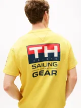 Remera amarilla de algodón con corte amplio, cuello redondo y hombros caídos. Presenta un logo pequeño de Tommy Hilfiger en el pecho, un logo en la manga y un logo grande en la espalda. Pertenece a la colección Hilfiger Sailing.