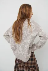 Buzo de tejido de punto en color marrón con un patrón ornamental floral en color celeste. Presenta cuello redondo, mangas largas y un corte holgado.