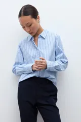 Camisa oversized de manga larga color celeste con rayas verticales finas en azul oscuro. Tiene cuello clásico y puños abotonados.