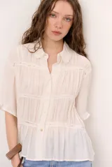 Camisa beige de manga corta con cuello camisero, detalles de encaje y cierre frontal con botones.