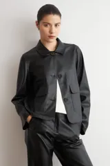 Chaqueta de cuero sintético negro con cuello camisero, cierre frontal de botones oscuros y bolsillos delanteros con solapa.