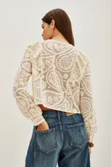 Saco corto de encaje color crema, con cuello redondo, mangas largas y volados en los hombros. Cierre frontal con botones dorados.