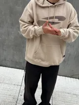 Canguro beige con capucha ajustable con cordones, bolsillo tipo canguro y estampado con diseño abstracto en negro.