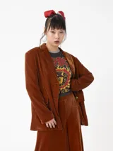 Blazer de terciopelo color marrón óxido, con solapas de muesca, un solo botón frontal dorado y bolsillos de parche.