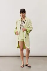Chaqueta oversize de gabardina color verde claro, con solapa clásica, bolsillos frontales, cierre de botones oscuros y mangas largas con vuelta en tono verde lima vibrante.