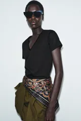 Cinturón tipo pañuelo de tejido satinado con estampado paisley en tonos rojos, azules, verdes y dorados sobre fondo negro. Presenta cierre con hebilla metálica y aplicación de tiras de piel.