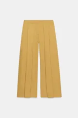 Jeans de tiro bajo y corte wide leg, color amarillo mostaza, con pliegues frontales, bolsillos ocultos y cierre frontal con cremallera, botón y ganchos metálicos.
