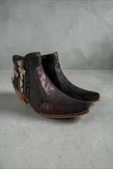 Botas de caña corta de cuero negro jaspeado, pintadas a mano con arte en tonos dorados, plateados y marrones en la parte trasera. Cuentan con doble cierre lateral con tiradores metálicos personalizados, puntera fina y taco cuadrado de madera.