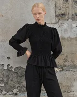 Blusa negra de lino con cuerpo y puños fruncidos, cuello alto con volados y mangas abullonadas.