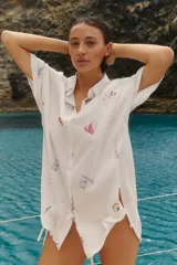 Camisa oversize de manga corta con cierre frontal de botones. Presenta un estampado integral con motivos náuticos y elementos gráficos.