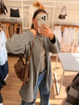 Cartera tipo baguette con estampado animal print, confeccionada en material suave símil gamuza. Presenta un bolsillo frontal con solapa y cierre, compartimento principal con cierre superior, y asa larga regulable de cuero sintético marrón.