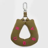 Charm para bolso o mochila de diseño acolchado en color verde oliva, con forma de herradura y la palabra 'BUBBA' bordada en hilo fucsia. Incluye un mosquetón metálico para colgar.