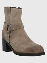 Bota corta de descarne color beige, con taco cuadrado y punta cuadrada. Presenta una correa con argolla metálica decorativa alrededor del tobillo y cierre lateral.