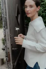 Buzo de punto color crema, con cuello polo y cierre frontal parcial con dos botones oscuros. Presenta mangas largas con puños acanalados y un diseño holgado.